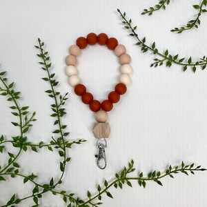 May include: A silicone beaded keychain with a wooden charm and a silver clip. The beads are in shades of orange, pink, and white.