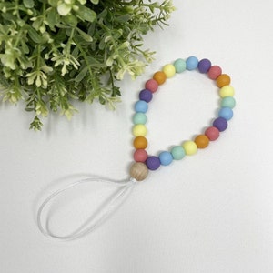 May include: A rainbow colored silicone beaded phone charm with a wooden bead and a white string.