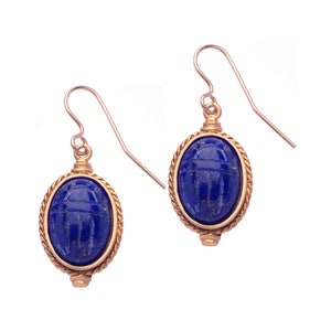 May include: A pair of gold earrings with a blue lapis lazuli stone carved with a scarab beetle design.