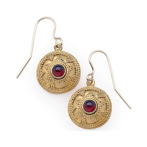 May include: A pair of gold earrings with a red gemstone in the center of each earring. The earrings have a circular design with a starburst pattern around the gemstone.