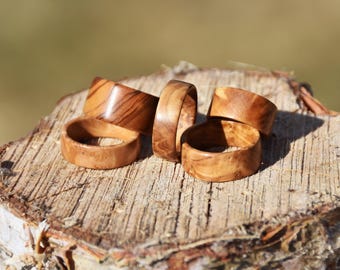May include: Five wooden rings stacked on a tree stump. The rings are made of light brown wood with a natural grain pattern.