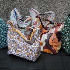 Peut inclure: Six sacs cabas à motifs différents dans des couleurs variées, notamment le vert, le bleu, le blanc, le marron et l'orange. Les sacs sont en tissu et présentent une variété de motifs, notamment des motifs géométriques, floraux et abstraits.