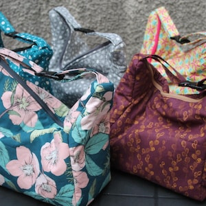 Peut inclure: Cinq sacs de courses réutilisables en tissu avec différents motifs. Les sacs sont tous pliés et empilés les uns sur les autres. Les motifs comprennent des pois, des fleurs et des motifs géométriques.