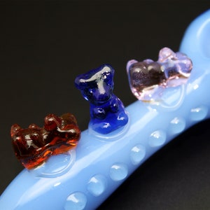 May include: A blue glass pipe with three glass bear figurines attached. The bears are red, blue, and pink.
