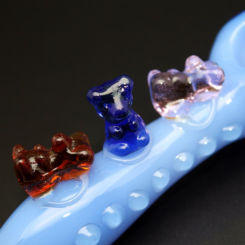 May include: A blue glass pipe with three glass bear figurines attached. The bears are red, blue, and pink.
