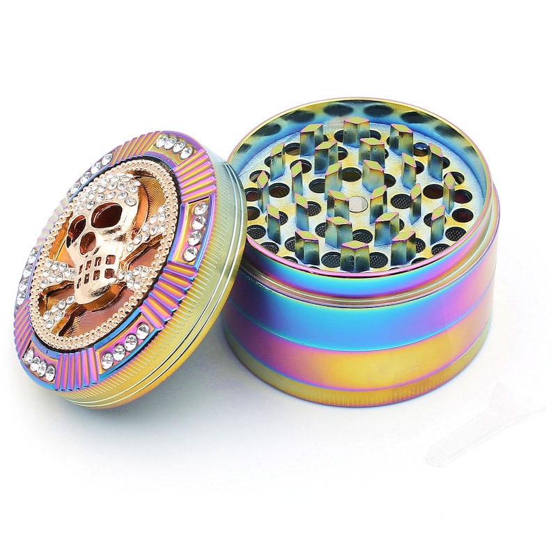 May include: A rainbow-colored grinder with a skull and crossbones design on the lid. The lid is adorned with clear rhinestones. The grinder is made of metal and has a multi-colored finish.