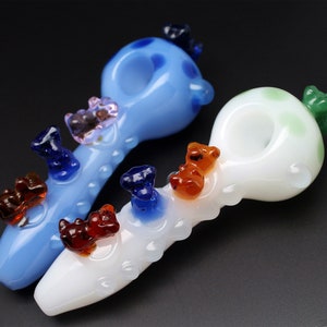 May include: Two glass smoking pipes with colorful bear figurines attached. One pipe is blue with white polka dots and the other is white with green polka dots.