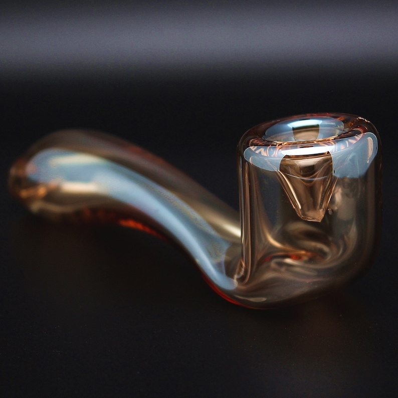May include: A clear glass pipe with a curved stem and a round bowl. The pipe has a light brown tint and is made of thick glass.