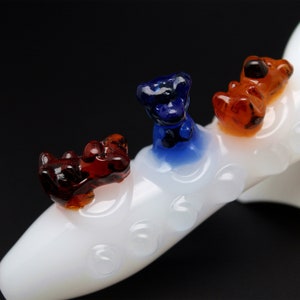 May include: White glass pipe with three small glass animal figurines on top. The figurines are orange, blue, and red.