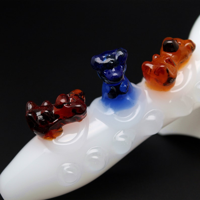 May include: White glass pipe with three small glass animal figurines on top. The figurines are orange, blue, and red.