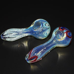 May include: Two glass smoking pipes with iridescent blue and white swirl designs. One pipe has a red and blue swirl design.
