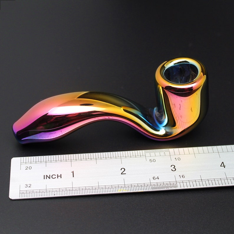May include: A rainbow iridescent glass pipe with a curved stem and a bowl. The pipe is about 3 inches long and is measured against a ruler.