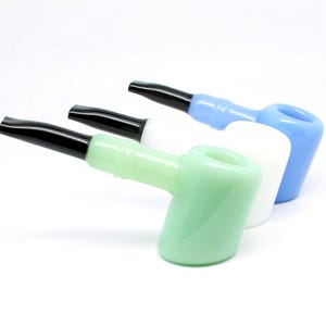 May include: Three glass pipes in a row, each with a different color. The first is light green, the second is white, and the third is light blue. Each pipe has a black mouthpiece and a rounded bowl.