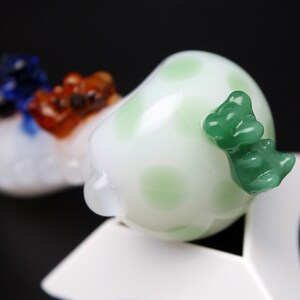 May include: White glass bead with green polka dots and a green glass animal figurine attached to the side.