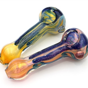 Puede incluir: Dos pipas para fumar de vidrio con remolinos y purpurina de colores. Las pipas están hechas de vidrio transparente con remolinos azules, amarillos y morados. Las pipas miden aproximadamente 12,5 cm de largo.