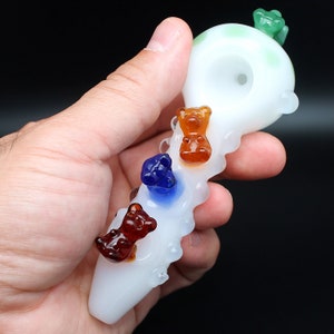 May include: White glass pipe with a wavy design and a round bowl. The pipe is decorated with four colorful gummy bear charms, including green, orange, blue, and brown.