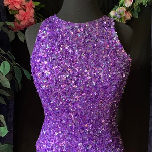 Puede incluir: Un top morado con lentejuelas y escote halter. Las lentejuelas son iridiscentes y crean un efecto brillante.