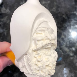 Può includere: Pipa in ceramica bianca con una scultura dettagliata di un viso di uomo barbuto con un cappuccio.