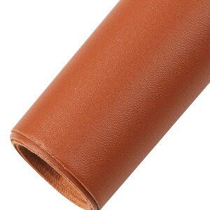 May include: Close-up of a rolled piece of brown faux leather. The leather has a textured surface.