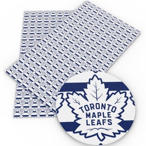 May include: White fabric with a repeating pattern of blue Toronto Maple Leafs logos. A larger blue Toronto Maple Leafs logo is in the centre of the image with white stripes.