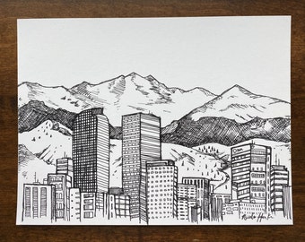May include: Black and white ink drawing of a city skyline with tall buildings and mountains in the background. The drawing is signed "Nicole Hank" in the bottom right corner.