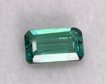 May include: A green emerald gemstone cut in a rectangular shape.