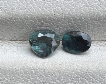 May include: Two faceted gemstones, one heart-shaped and one oval, both with a dark blue-green color.