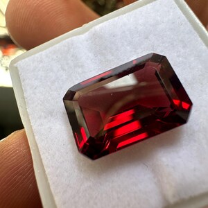 Puede incluir: Una piedra preciosa de color rojo intenso con un corte rectangular, expuesta sobre un fondo blanco.