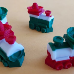 May include: Four miniature toy train engines painted in the colors of the Mexican flag, each with a green, white, and red stripe and a sombrero on top.
