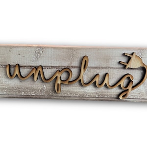 May include: Wooden sign with the word "unplug" in a cursive font, and a wooden plug design. The sign is mounted on a distressed, light gray wooden plank.