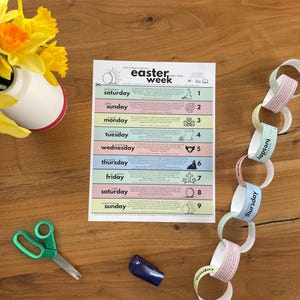 May include: A colorful Easter week chart with days of the week and corresponding illustrations. A paper chain with days of the week is next to the chart. A pair of green scissors, a blue object, and a vase of yellow flowers are also on the wooden surface.