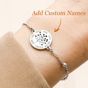 Puede incluir: Una pulsera de plata con un dije redondo que presenta un árbol con corazones y nombres a su alrededor. Los nombres en el dije son "Wyatt", "Chris", "Cynthia", "William", "Tyler", "Mama", "George".