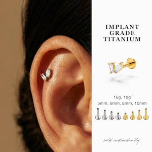 Puede incluir: Un pendiente de titanio dorado con una piedra blanca de forma rectangular y ovalada. La imagen también muestra el texto "IMPLANT GRADE TITANIUM" y los tamaños 5 mm, 6 mm, 8 mm y 10 mm.