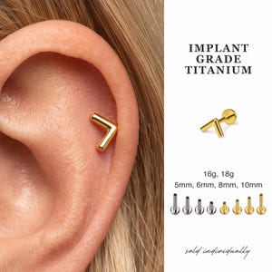 May include: A gold-colored chevron-shaped stud earring made of implant grade titanium. The text reads IMPLANT GRADE TITANIUM, 16g, 18g, 5mm, 6mm, 8mm, 10mm, and sold individually. Eight flat-back posts are shown in silver and gold tones.