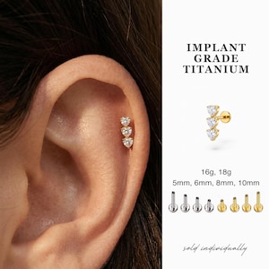 May include: Gold-colored ear piercing jewelry with three heart-shaped clear stones. The image includes the text "IMPLANT GRADE TITANIUM" and size options: 16g, 18g, 5mm, 6mm, 8mm, and 10mm. The text "sold individually" is also present.