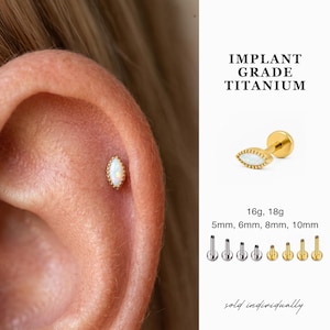 May include: An implant grade titanium flat back stud earring featuring a marquise-cut white opal stone with a beaded gold-tone border. The text reads IMPLANT GRADE TITANIUM, 16g, 18g, 5mm, 6mm, 8mm, 10mm, and sold individually. Includes various post lengths.