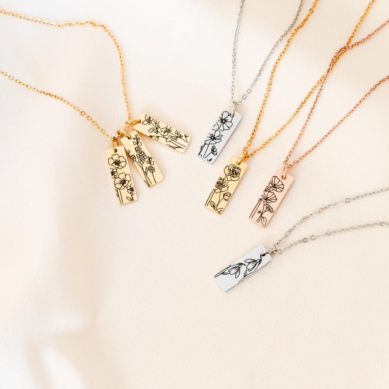 May include: Four delicate necklaces with floral pendants. Each necklace features a different chain style and a rectangular pendant with a delicate floral design. The pendants are in gold, rose gold, and silver.
