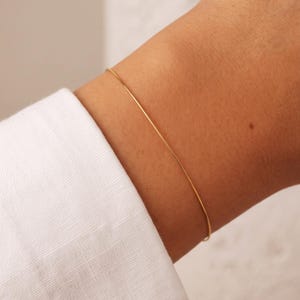 May include: A thin, smooth gold bangle bracelet worn on the wrist. The bracelet is a simple, continuous circular band with a polished metallic finish. The text "© CelestialbyA&J. All rights reserved" is printed at the bottom of the image.