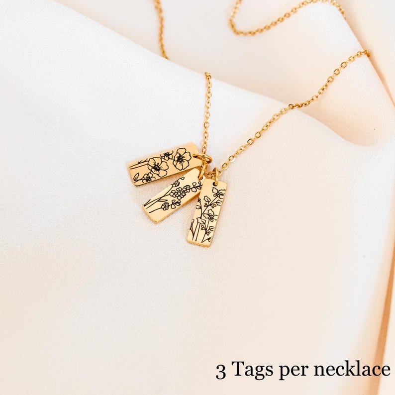 May include: Gold necklace with three rectangular tags, each featuring a delicate floral design. The tags are connected to the chain with jump rings. 3 Tags per necklace.