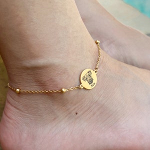 May include: Gold ankle bracelet with a round charm featuring a dog's face and the name "Fox" engraved on it.