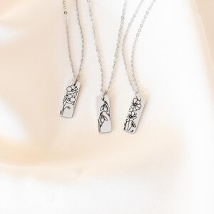 May include: Three silver necklaces with delicate flower pendants. Each pendant features a different floral design, including a single flower, a cluster of flowers, and a single flower with leaves.
