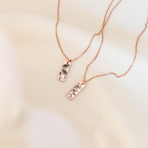 May include: Two rose gold necklaces with delicate chains and rectangular pendants featuring a floral design.
