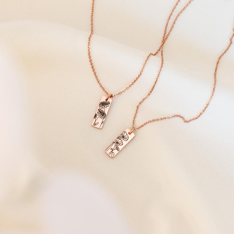 May include: Two rose gold necklaces with delicate chains and rectangular pendants featuring a floral design.