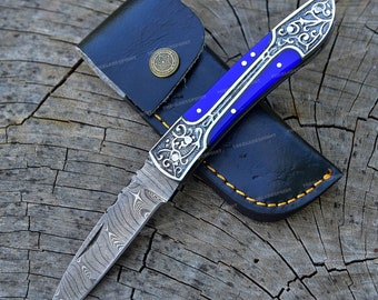 May include: A blue and silver pocket knife with a decorative handle and a Damascus steel blade. The knife is in a black leather sheath.