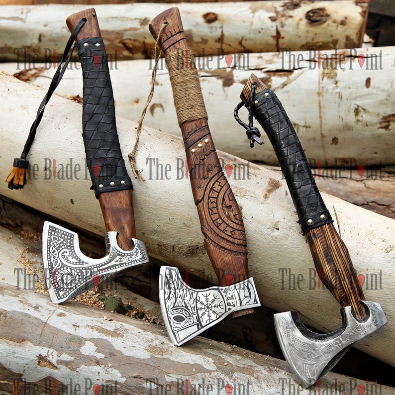 May include: Three Viking axes with wooden handles and metal axe heads. The handles are wrapped in leather or rope. The axe heads feature intricate designs. The axes are displayed on a wooden surface.