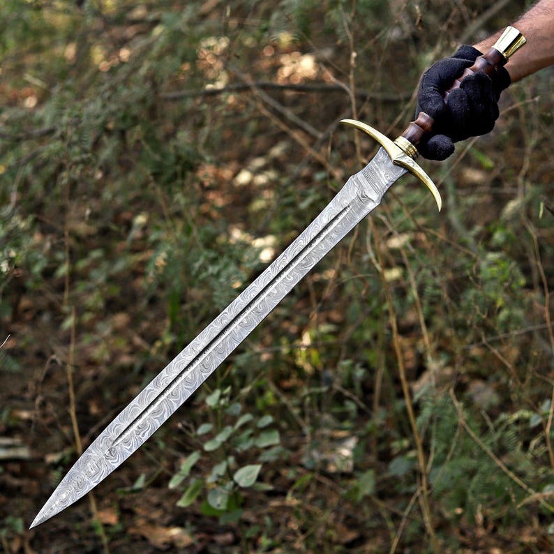 May include: A double-edged sword featuring a patterned Damascus steel blade, a brass crossguard, and a dark wooden handle with a brass pommel. The blade displays a distinct wavy, layered metal texture running along its length to a sharp point.