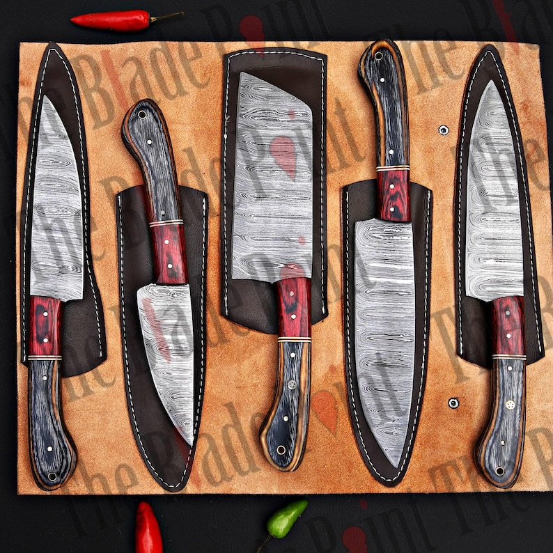 Pu&ograve; includere: Set di cinque coltelli da cucina con lame in acciaio damascato e manici in legno. I coltelli sono esposti in foderi di cuoio su uno sfondo marrone.