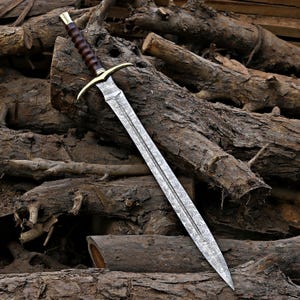May include: A sword with a patterned Damascus steel blade, a brass crossguard, and a dark brown ridged wooden handle. The blade features a central fuller and a sharp point, while the hilt includes a brass pommel cap at the end.