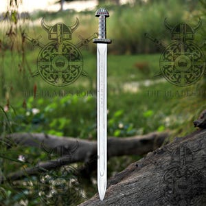 May include: A double-edged steel sword featuring a straight blade with a central fuller and a pommel decorated with small red circular inlays. The hilt has a textured grip, and the blade displays engraved runic-style characters.
