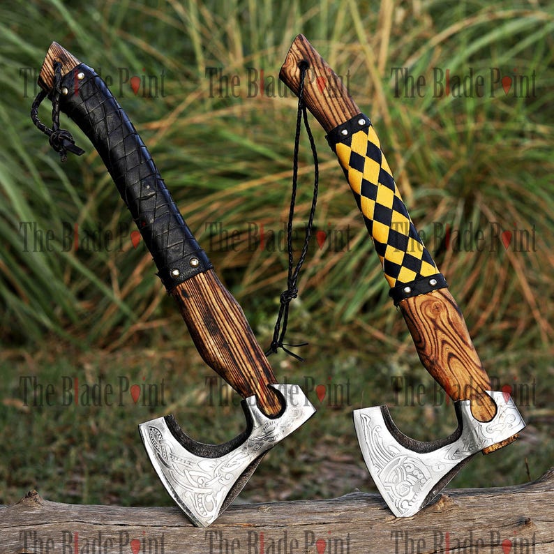 May include: Two Viking axes with wooden handles and silver blades. One axe has a black leather-wrapped handle, the other has a yellow and black checkered grip. Both axes have a decorative design on the blade.